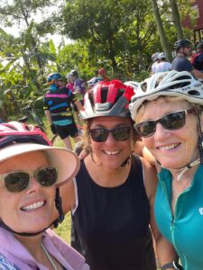Three Women in Cycling Hats and Sunglasses with Trees Behind Them